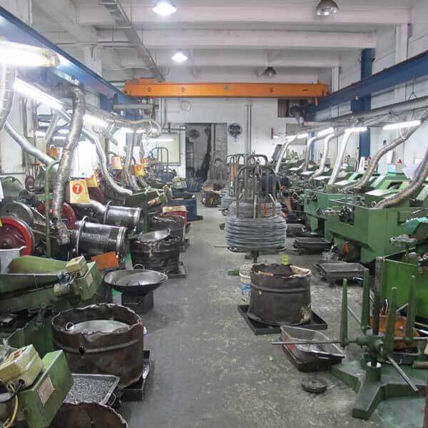 Two rows of heading and thread rolling machines, with coiled wire down the centre aisle and an overhead crane